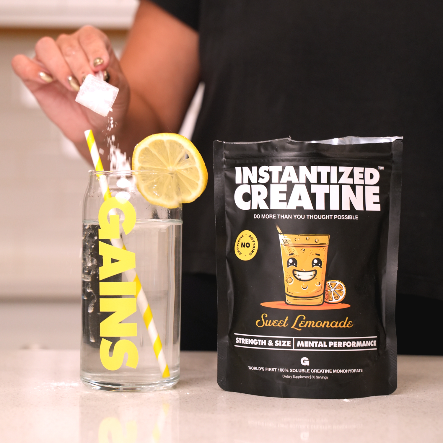 Person adding powder to a glass of water with a creatine supplement package next to it.