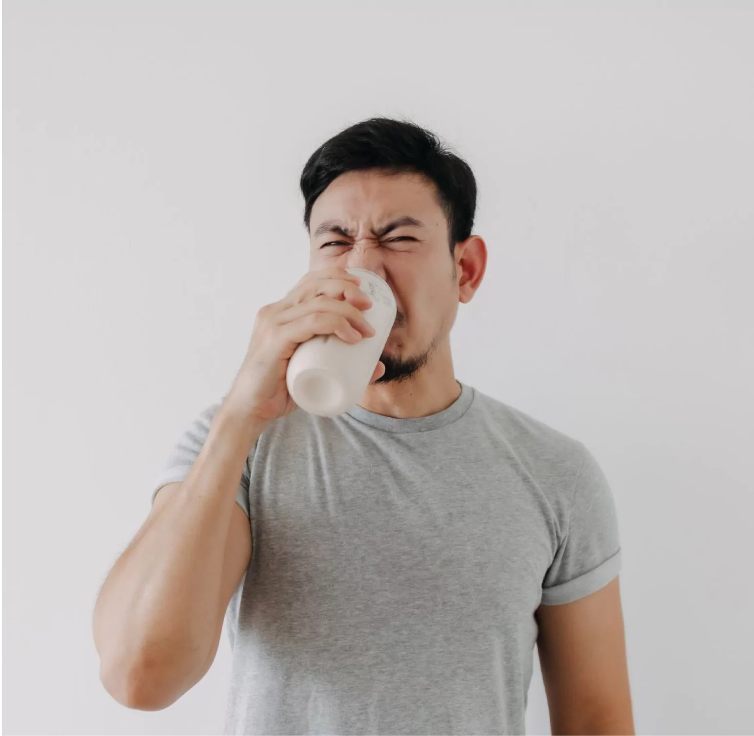 Man in a gray shirt grimacing while drinking from a cup.