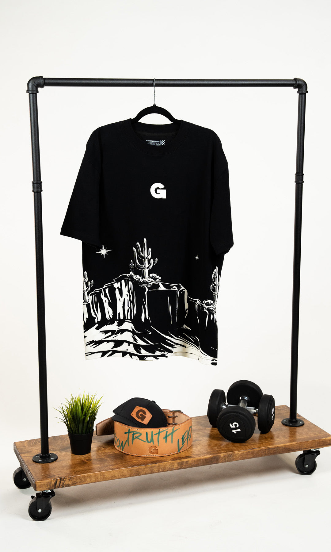 Black t-shirt with desert scene, hat, belt, and dumbbells on a wooden rack.