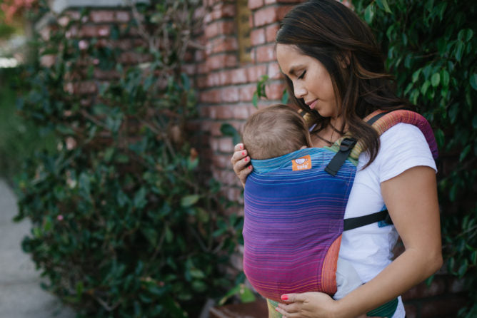 Une mère portant son enfant dans un porte-bébé Signature de Tula.