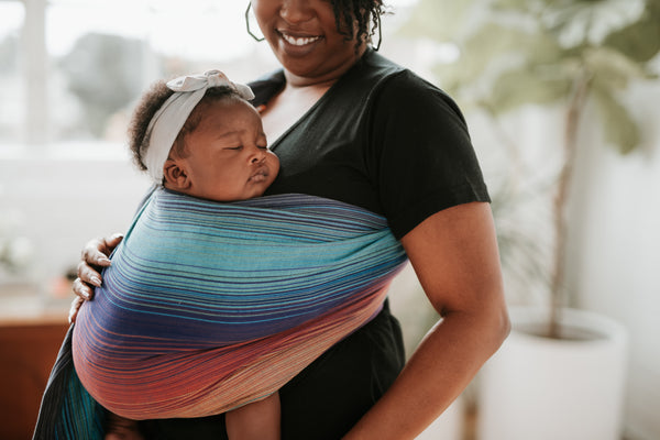 Une mère portant son enfant endormi dans une écharpe de portage.