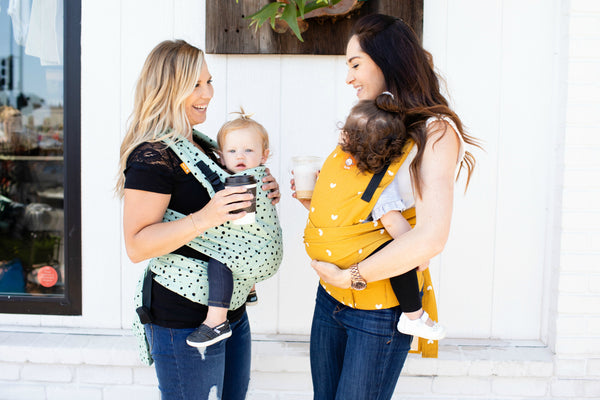 Two mothers carrying their children in baby carrier.