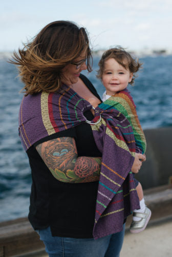 Eine glückliche Mutter und ihr Kind nutzen einen Ring Sling, während sie am Meer sind.