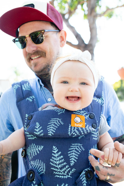 Un père et son enfant souriant utilisant un porte-bébé Tula en position de portage face à l'avant.