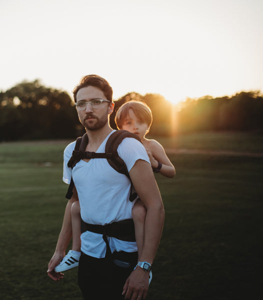 Un père portant son fils en position de portage sur le dos.