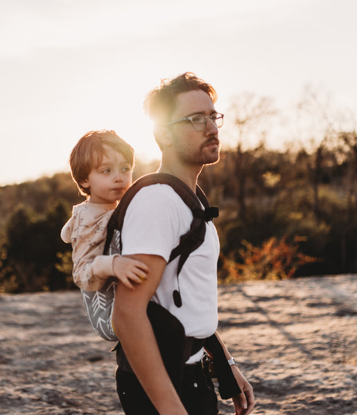 Un père portant son fils en position de portage dorsal dans la nature.