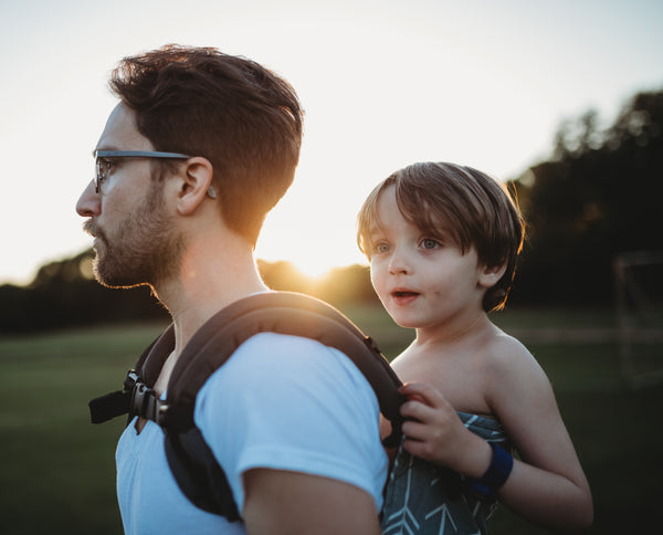 Un père portant son fils en position de portage sur le dos.