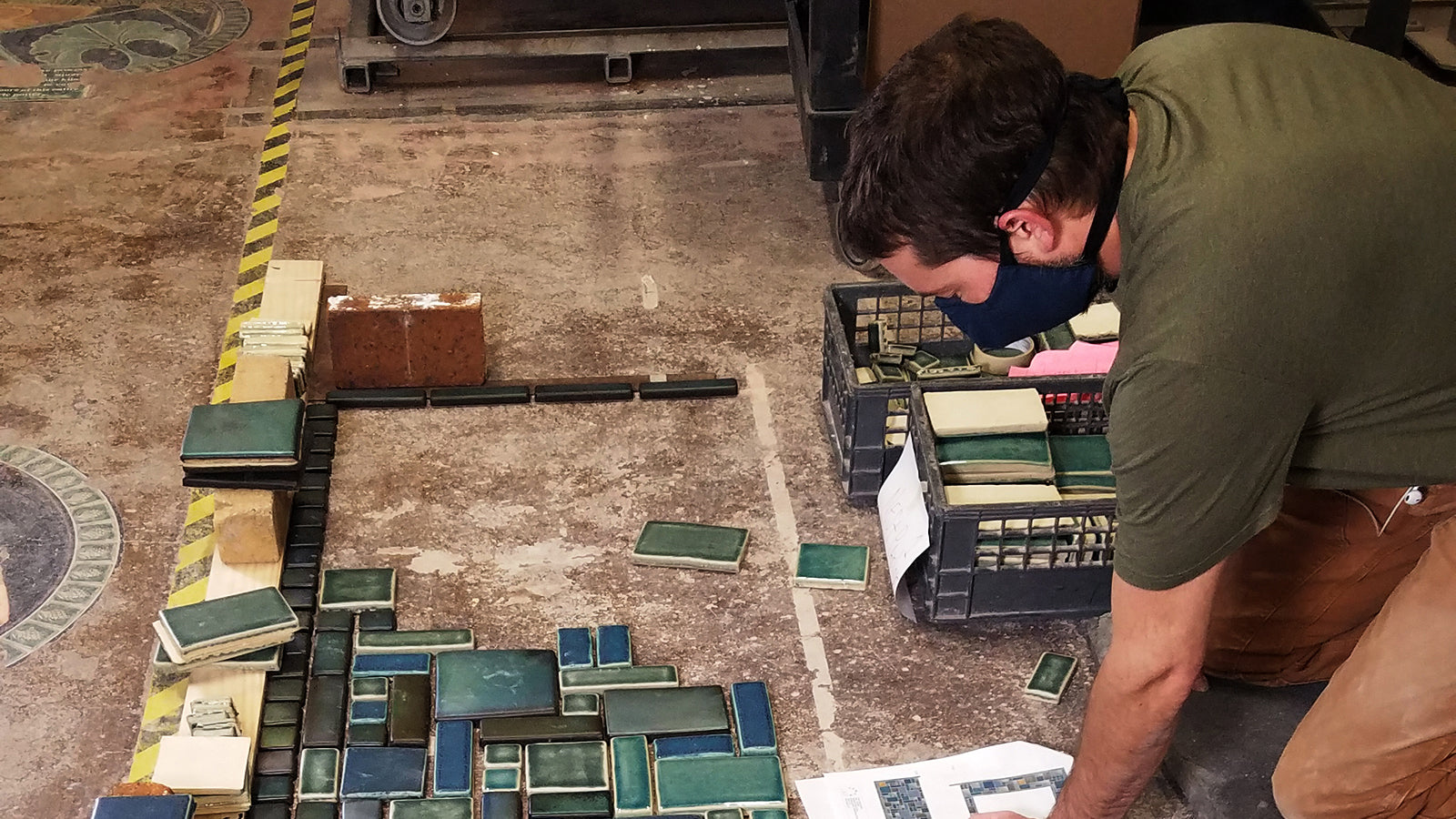 Man wearing a mask in green planning the layout of green Pewabic tile at Pewabic Pottery