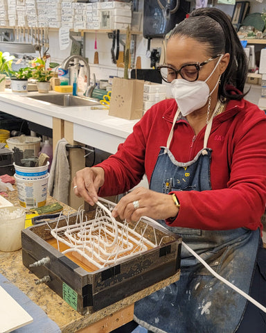 Master Mold Maker Sherlyn working in the studio. She is wearing a red shirt and a denim Pewabic apron. She wears her hair in a high pony tail.