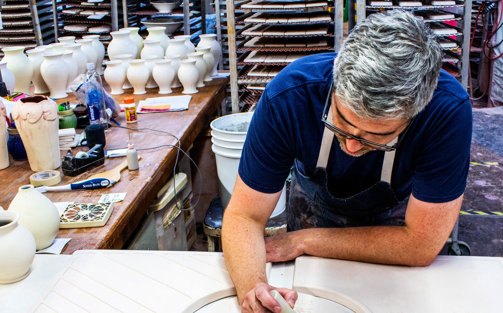 Pewabic artist hand-painting a large custom piece for a client. The artist is in a studio surrounded by vessels and tiles waiting to be glazed.