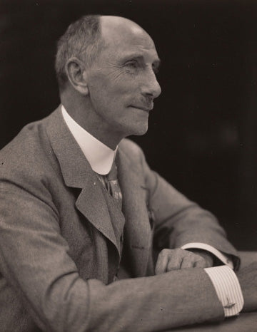 Sepia-toned portrait of American Industrialist, Charles Lang Freer. He is wearing a light suit, his hands are casually folded in front of him, and he has a relaxed smile on his face.