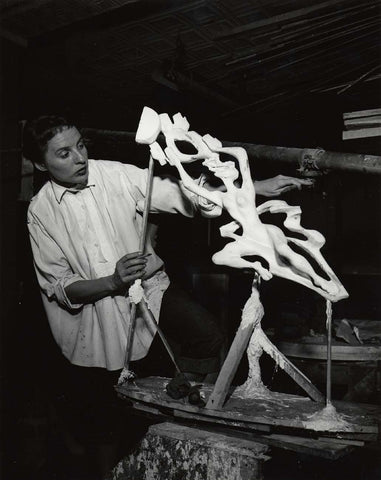 Gwen Lux in her studio–– photographed by Peter A. Juley & Son. Lux is wearing an oversized, white-collared shirt and working on an abstract sculpture using a light clay body.