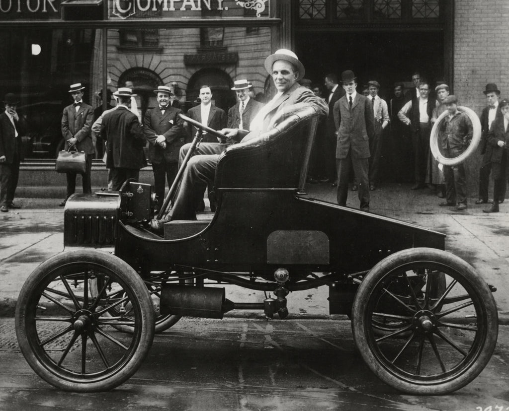 Henry Ford taking a ride in a Ford Model A, 1904. There are men standing behind him admiring the vehicle.