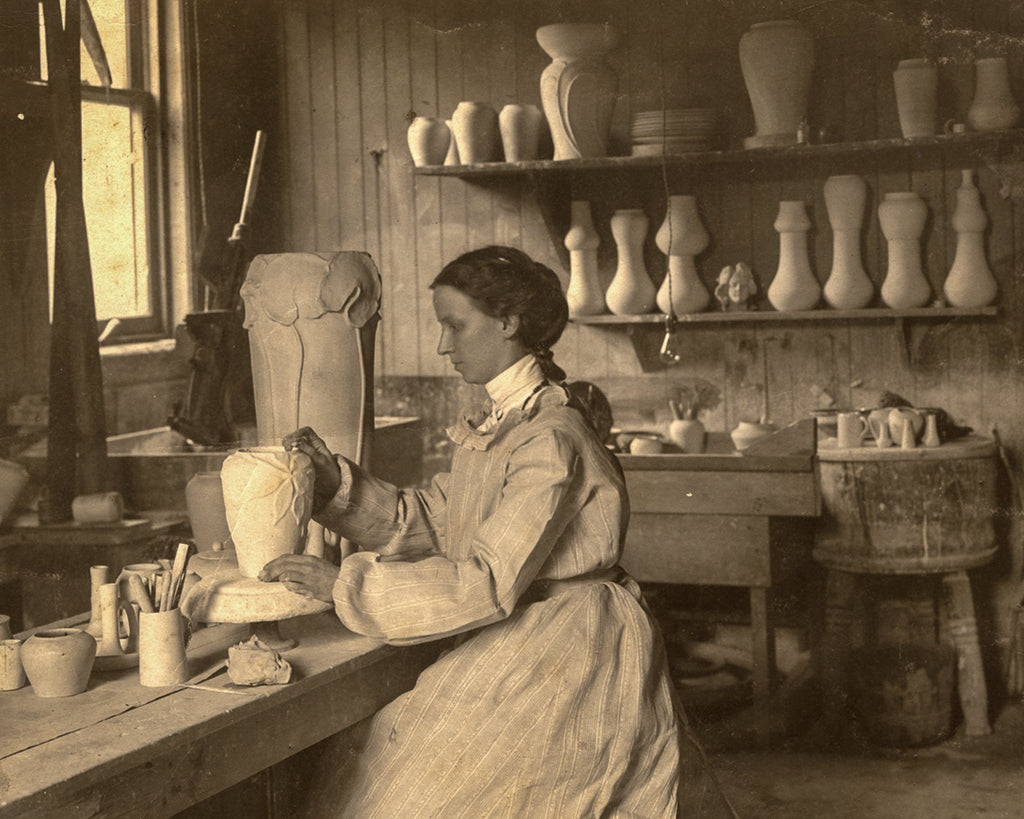 Sepia film photo scan of Mary Chase Perry Stratton sitting in a long gown, putting the finishing touches on a vase in the Stable Studio circa 1904.