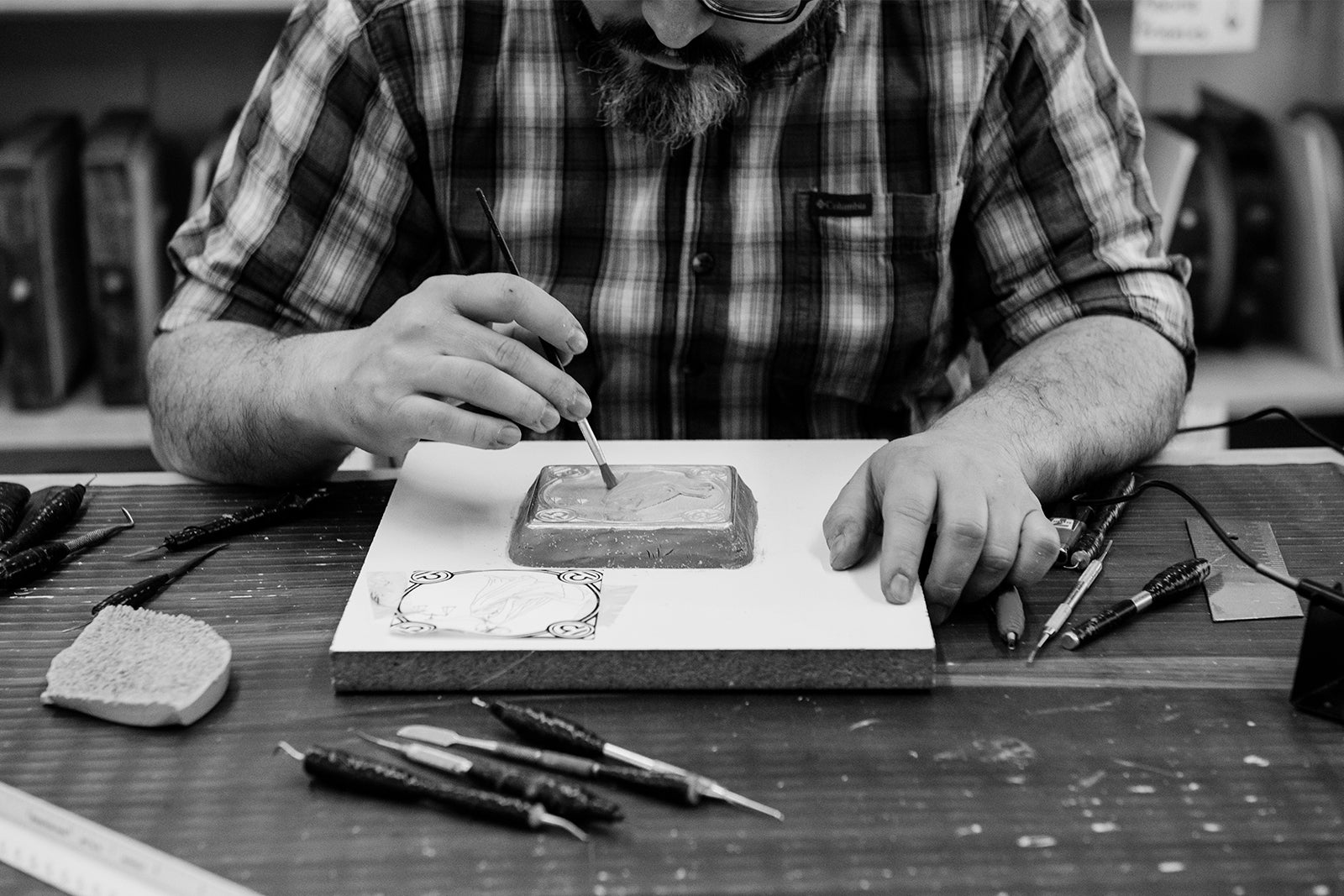 Black and white photo of Designer Chris meticulously sculpting one of the tiles included in our ongoing Zodiac Collection