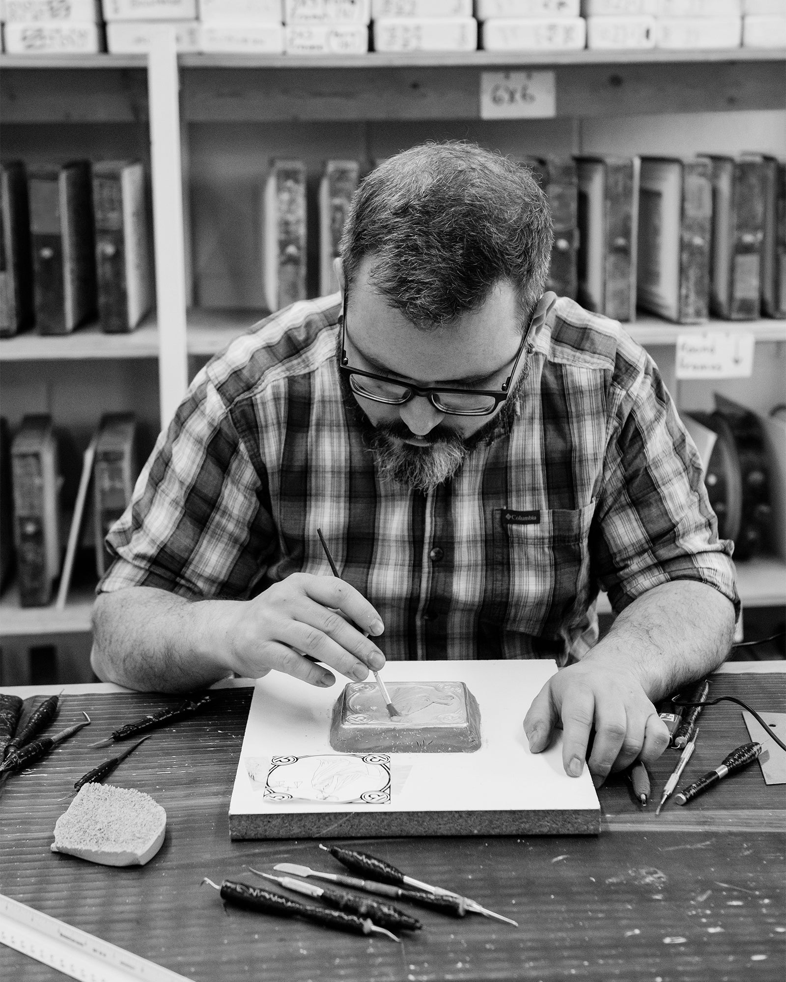 Black and white photo of Pewabic Designer Chris hand-sculpting a portion of a tile included in our ongoing Zodiac tile series.