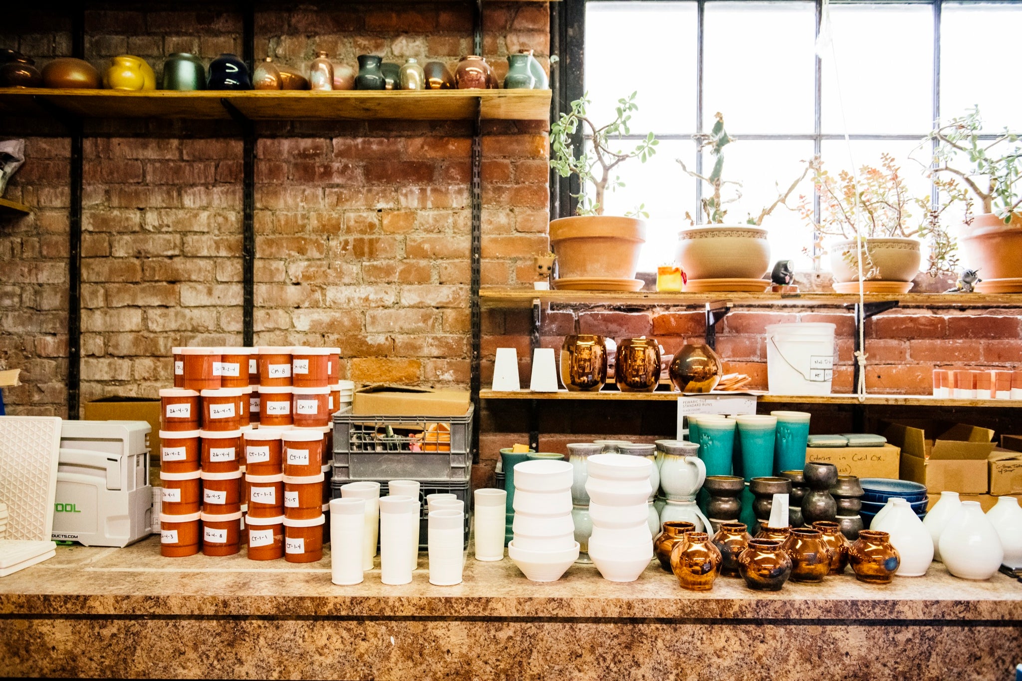 Snapshot of Pewabic Glaze Development Specialist Alex's office. There are various vessels and glaze containers on the working desk.