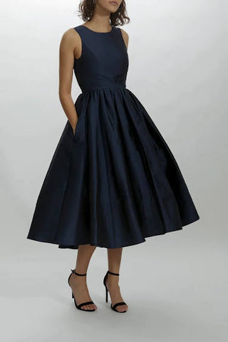 Knee length boat neck dress with open back and bow belt detail, shown in navy.