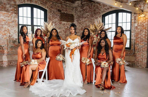 Bride wearing white dress posing with eight bridesmaids in orange dresses