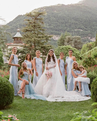 Bride in white dress posing with seven bridesmaids in light blue dresses and a flower girl in a white dress.