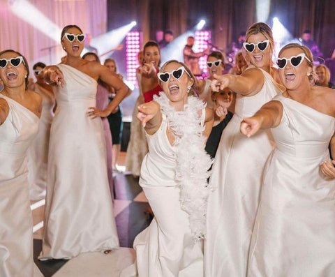 Bridesmaids dancing at reception wearing white dresses and sunglasses