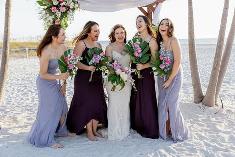 Bride in white surrounded by her four bridesmaids in various shades of blue on a beach.