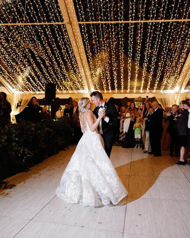 A bride and groom on the dance floor having their first dance under many gorgeous string lights.