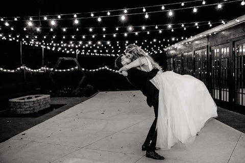 Groom lifting and kissing the bride, black and white picture on a dance floor at night under string lights.