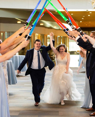 Bride and groom walking through Frederik Meijer Gardens wedding venue with bridal party holding toy lightsaber swords over the couple's heads