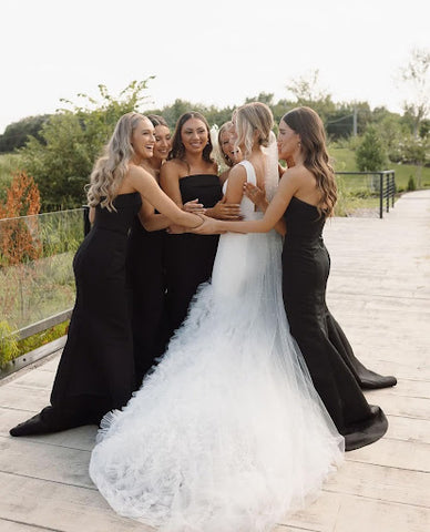 Five beautiful women in black dresses hugging a blonde bride