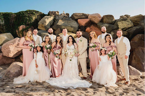 Bride and groom with full wedding party in front of a rock wall on the beach.
