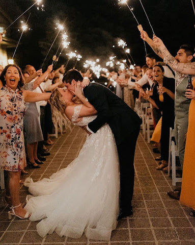 Bride and groom kissing while guests cheer with sparklers.