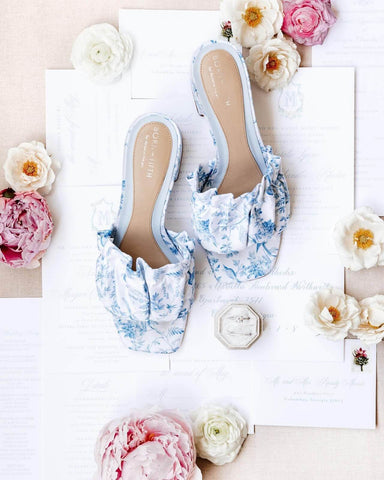 Women's wedding shoes displayed on a table with flowers and wedding invitation suite