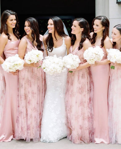 Five bridesmaids in pale pink surround the bride in white, everyone is holding white bouquets and smiling.