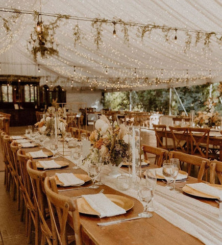 rustic tables and chairs set for rehearsal dinner in a tent under string lights and greenery