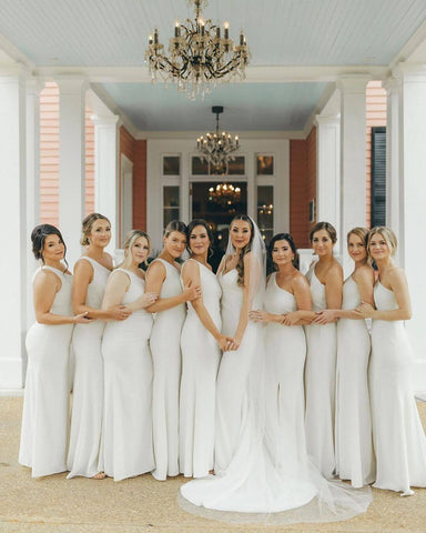 Group of bridesmaids posing in white dresses. One bridesmaid is pregnant