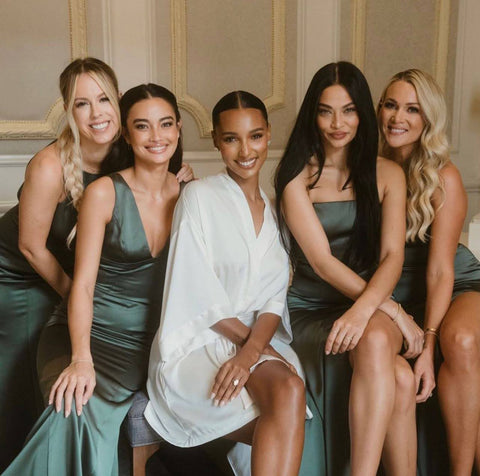 A bride in a white robe sits smiling with her four bridesmaids in green around her.