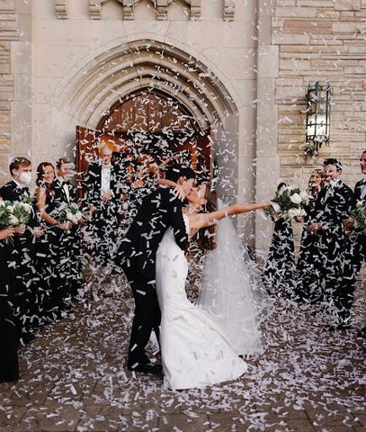 Bride and groom kissing outside a church while guests throw confetti.