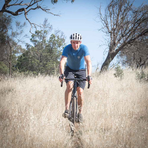 Morgan riding a bike through tall dry grass, wearing an ioMerino Cycling Jersey.