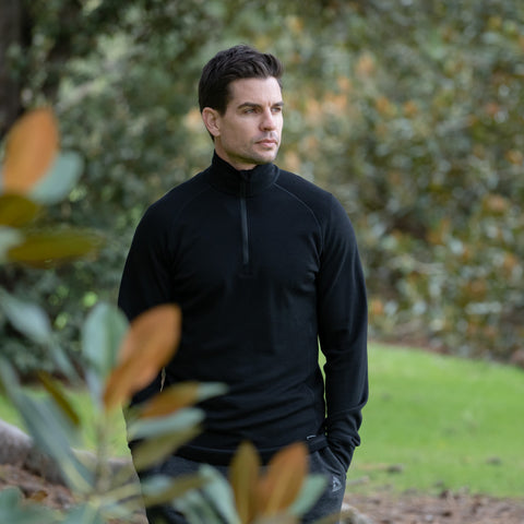 Model wearing ioMerino's Men's Pinnacle 2.0 in Black, standing amongst shrubbery