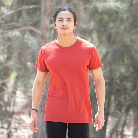 Model wearing ioMerino's Men's Universal Tee in Chilli, walking on a trail.