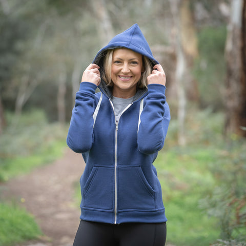 Model wearing ioMerino's Women's Summit Zip Hoodie in Patriot Blue, standing on a trail
