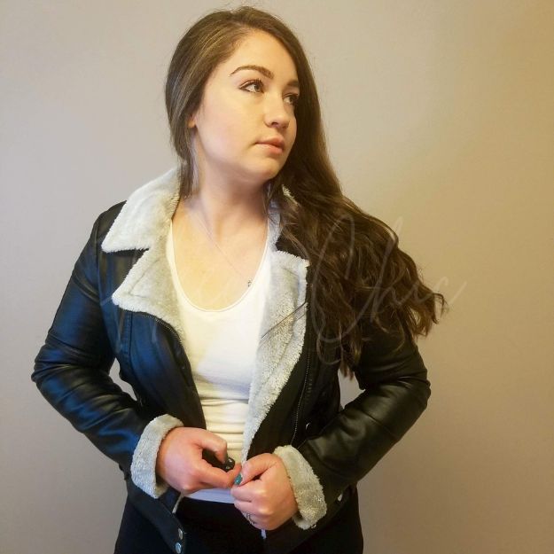 Leather and fur jacket by Fleece Chic is worn by a woman in black pants with long brown hair.