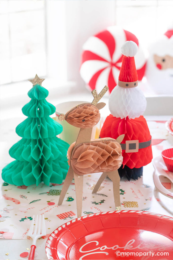 A close up of a festive Christmas cookie decorating party table featuring Momo Party's Cookies for Santa red round plates and Christmas character honeycomb featuring Santa, Christmas trees and reindeers.