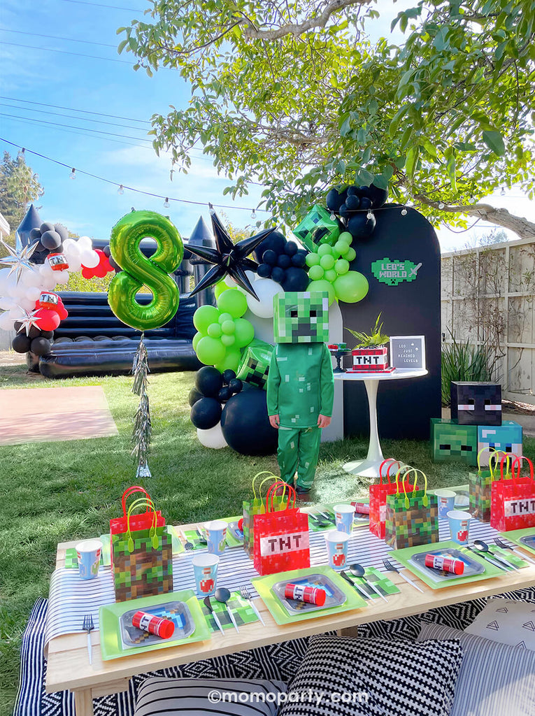 Minecraft themed Birthday Party Ideas by Momo Party. Party-set-up with backdrop, kids table, and birthday boy wearing creeper costume