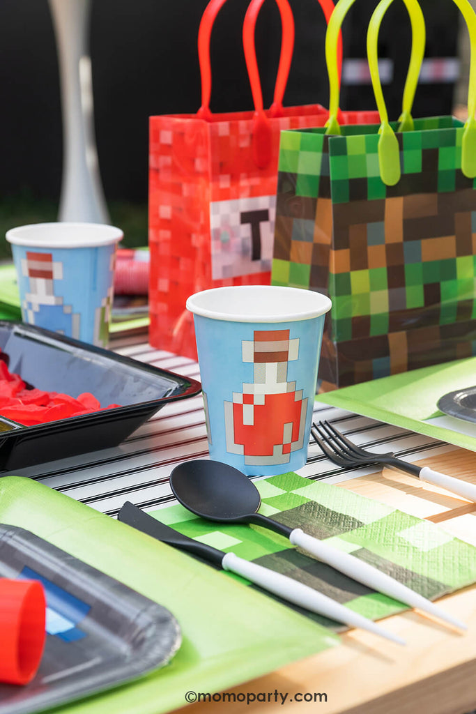 Minecraft themed Birthday Party Ideas by Momo Party. Featuring blue Minecraft potion paper cup with image of a potion bottle print, Minecraft gray side plate and modern sophisticated large lime green dinner plates, beautiful black and white cutlery sets, an pixel TNT theme goodie bags, all on the black striped table runner of the kids picnic table.