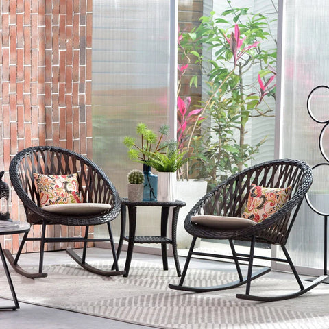 Two black wicker rocking chairs with beige cushions and floral pillows sit on a rug in a sunroom.