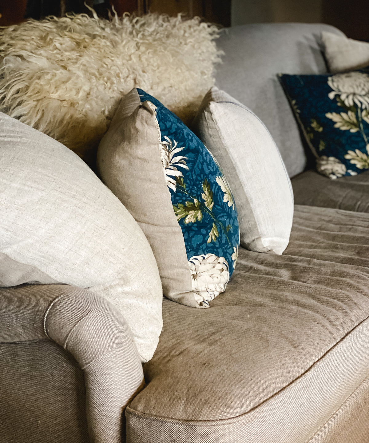 Floral and white throw pillows on a couch, felted sheep rug draped over the back of couch.