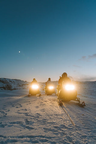Three snowmobiles travelling at dusk.