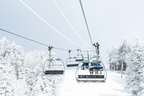 A ski lift with multiple chairs ascending and desceding over a snowy landscape dotted with frosted trees under a bright, clear sky.